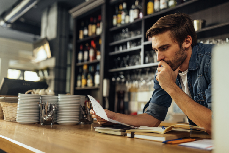 A man behind the counter of a restaurant looking at an invoice. 