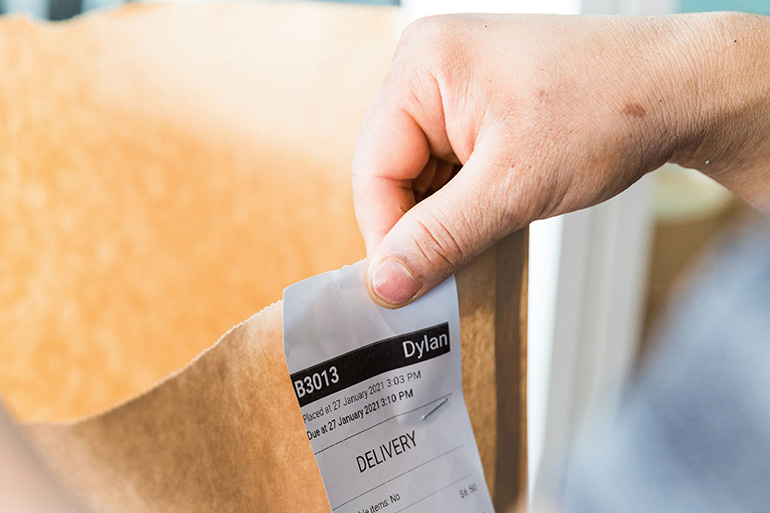 A closeup of a person's hand holding a food delivery bag.